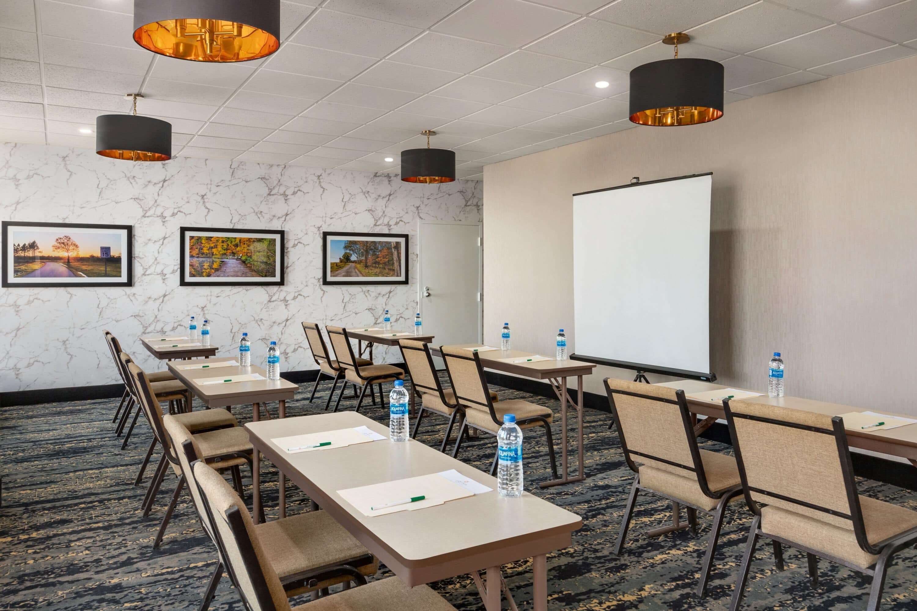 A conference room with tables, chairs, water bottles, and a projector screen.