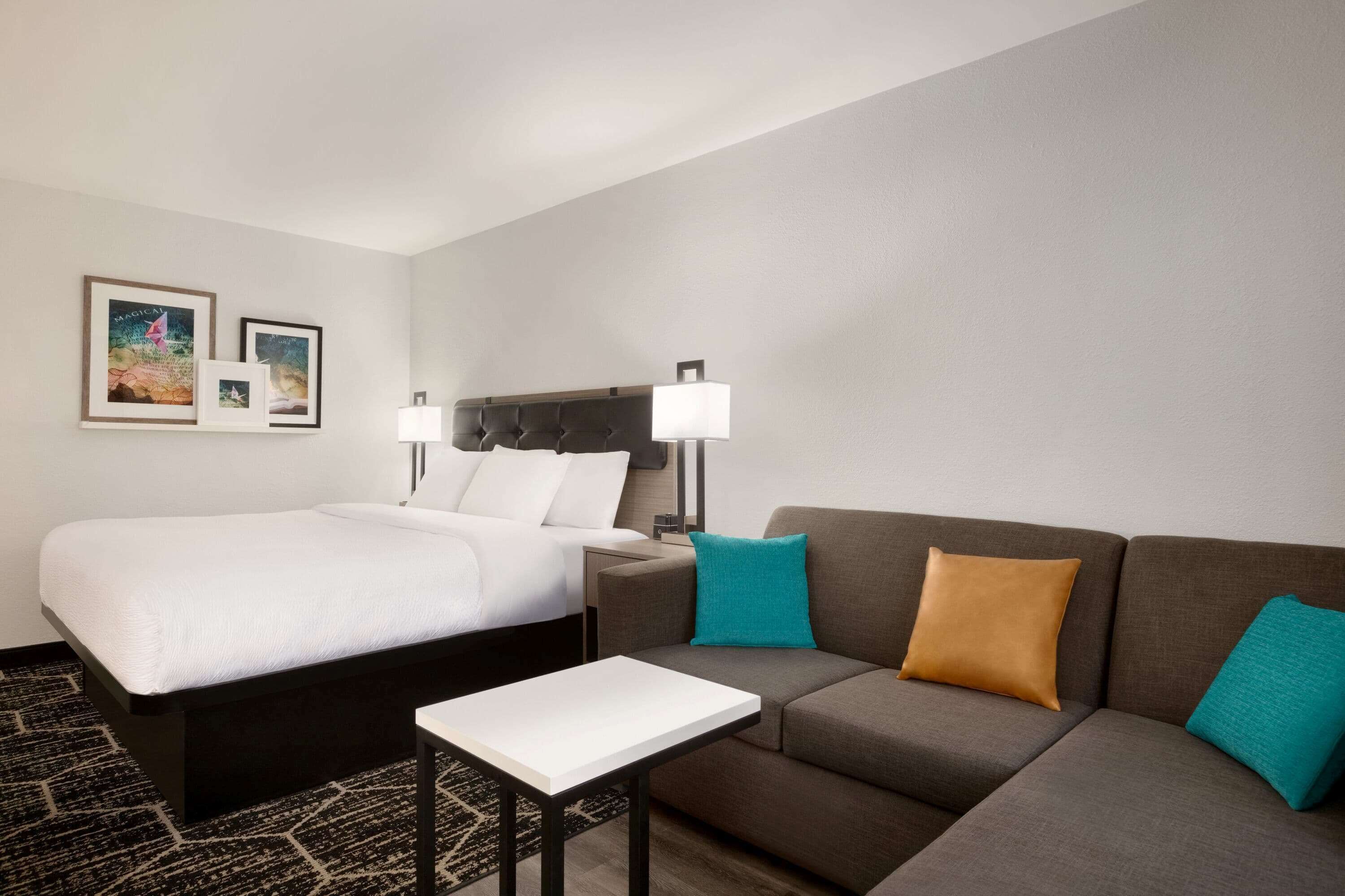 Una habitación de hotel con una cama, un sofá, una mesita y dos lámparas fijadas a la pared.