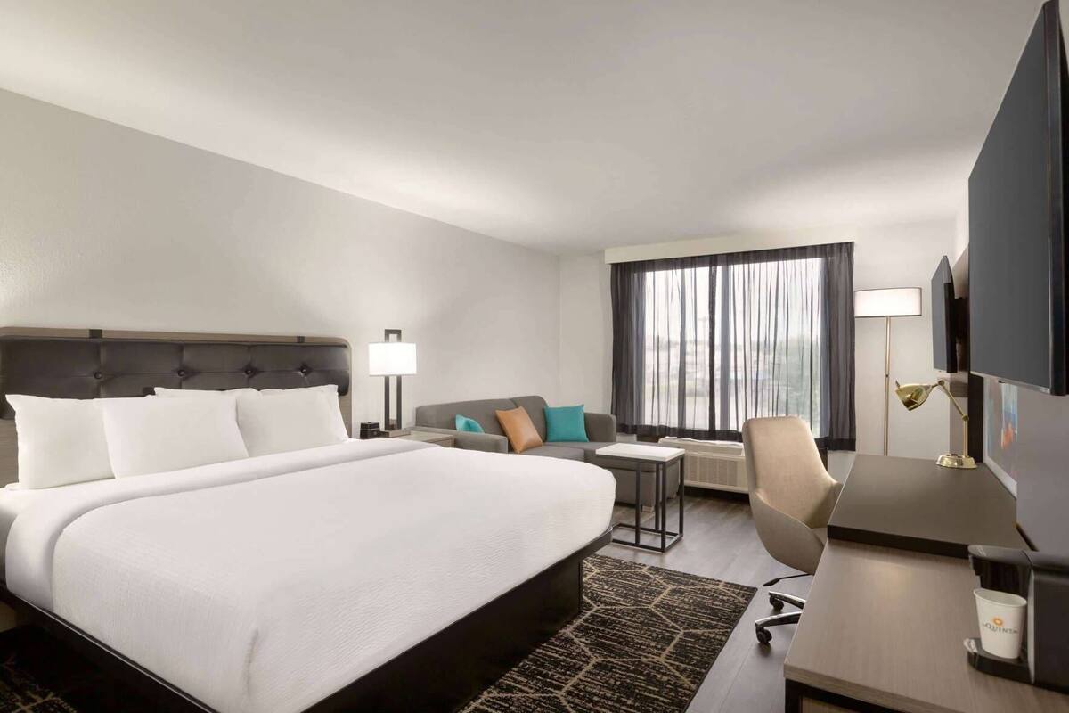 A hotel room with a large bed, a desk, a chair, a sofa, and a TV.