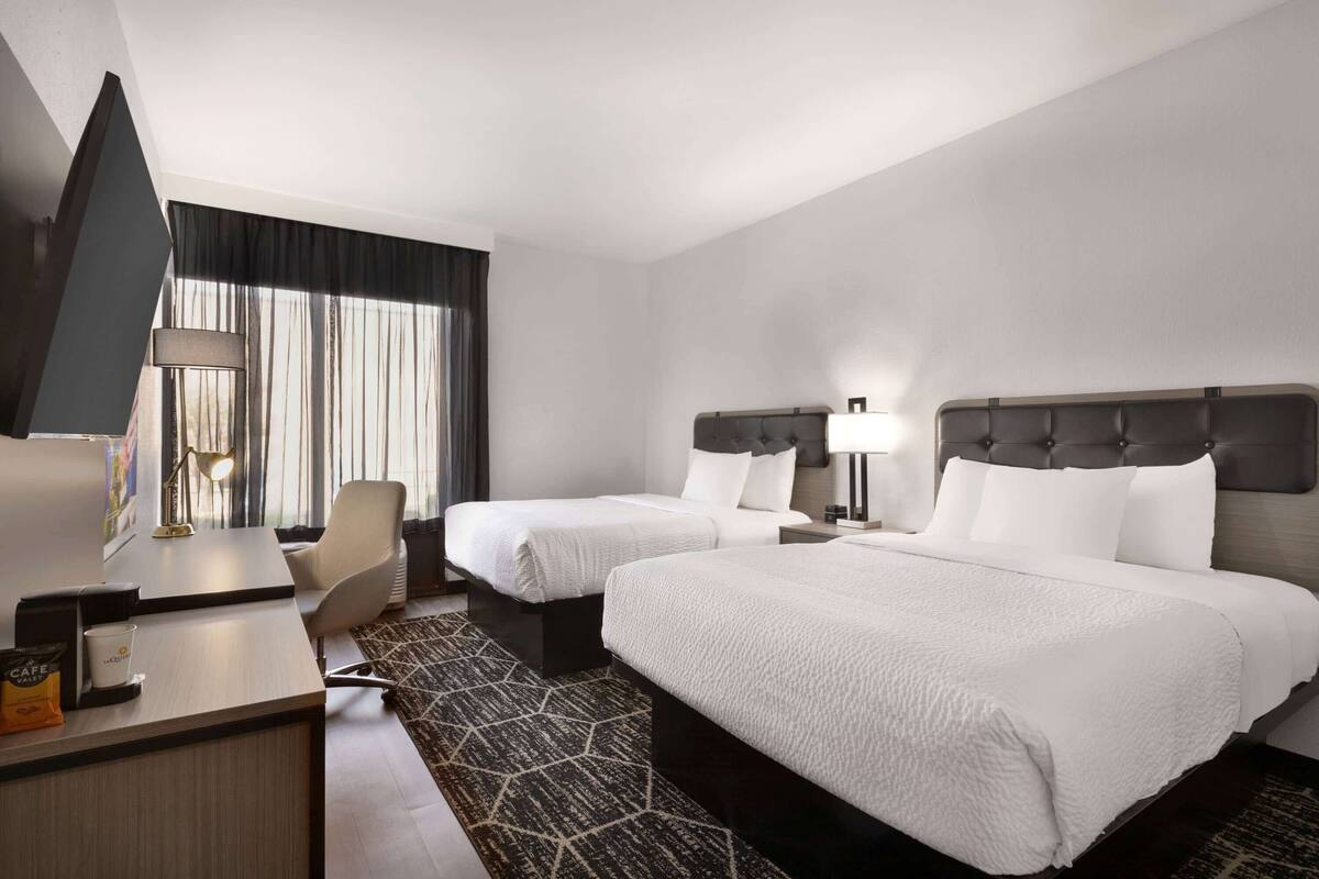 A hotel room with two beds, a desk, a TV, and a window with curtains.
