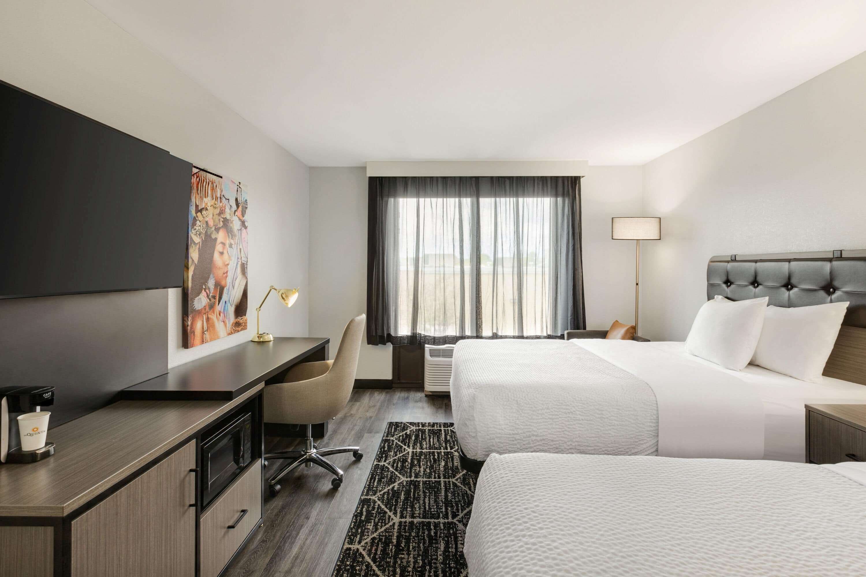 A hotel room with a bed, a desk, a chair, a TV, and a window with curtains.