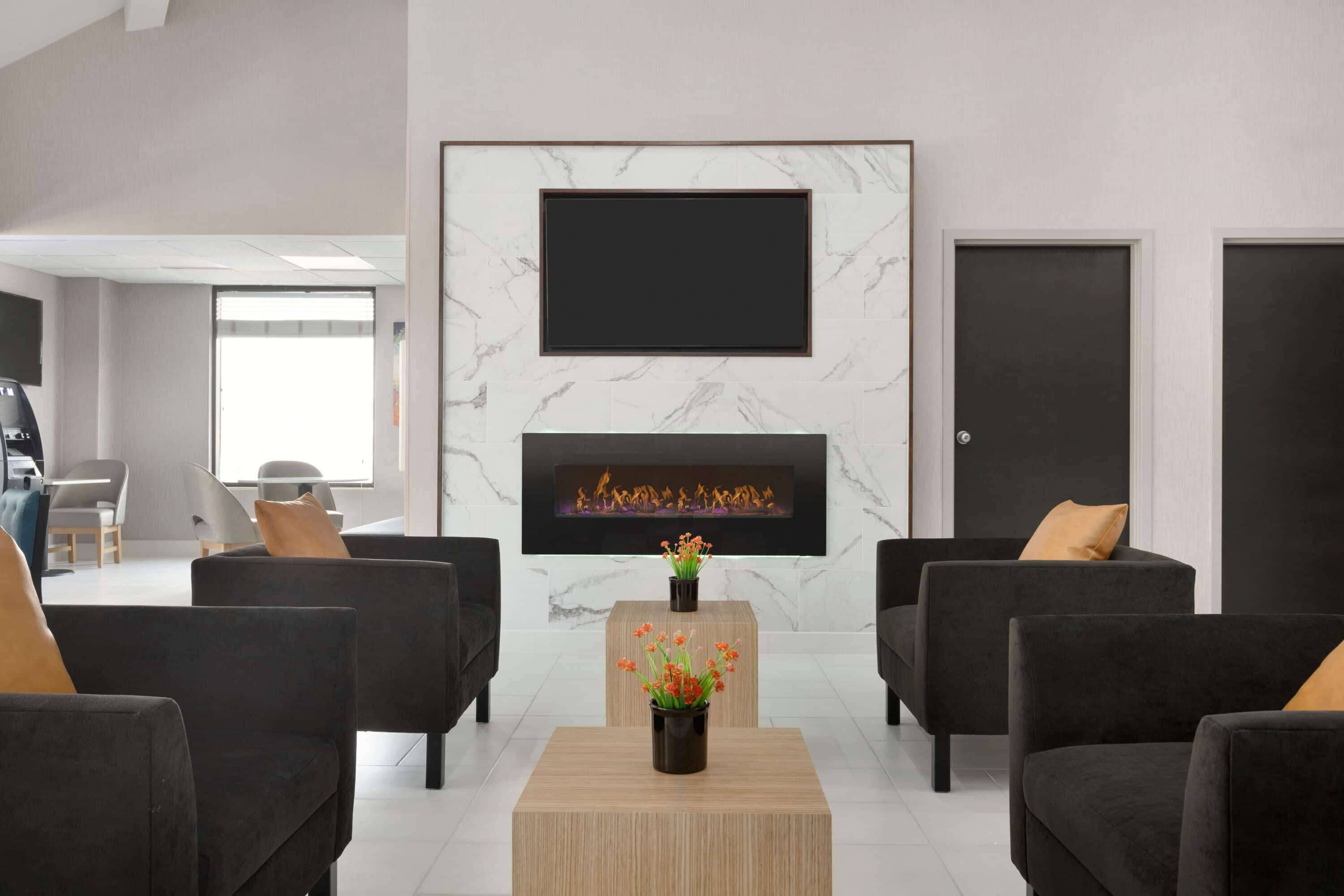 Een moderne woonkamer met een open haard, zwarte banken en een bijzettafeltje met bloemen.