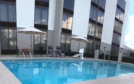 A modern building with a swimming pool, outdoor seating, and umbrellas.
