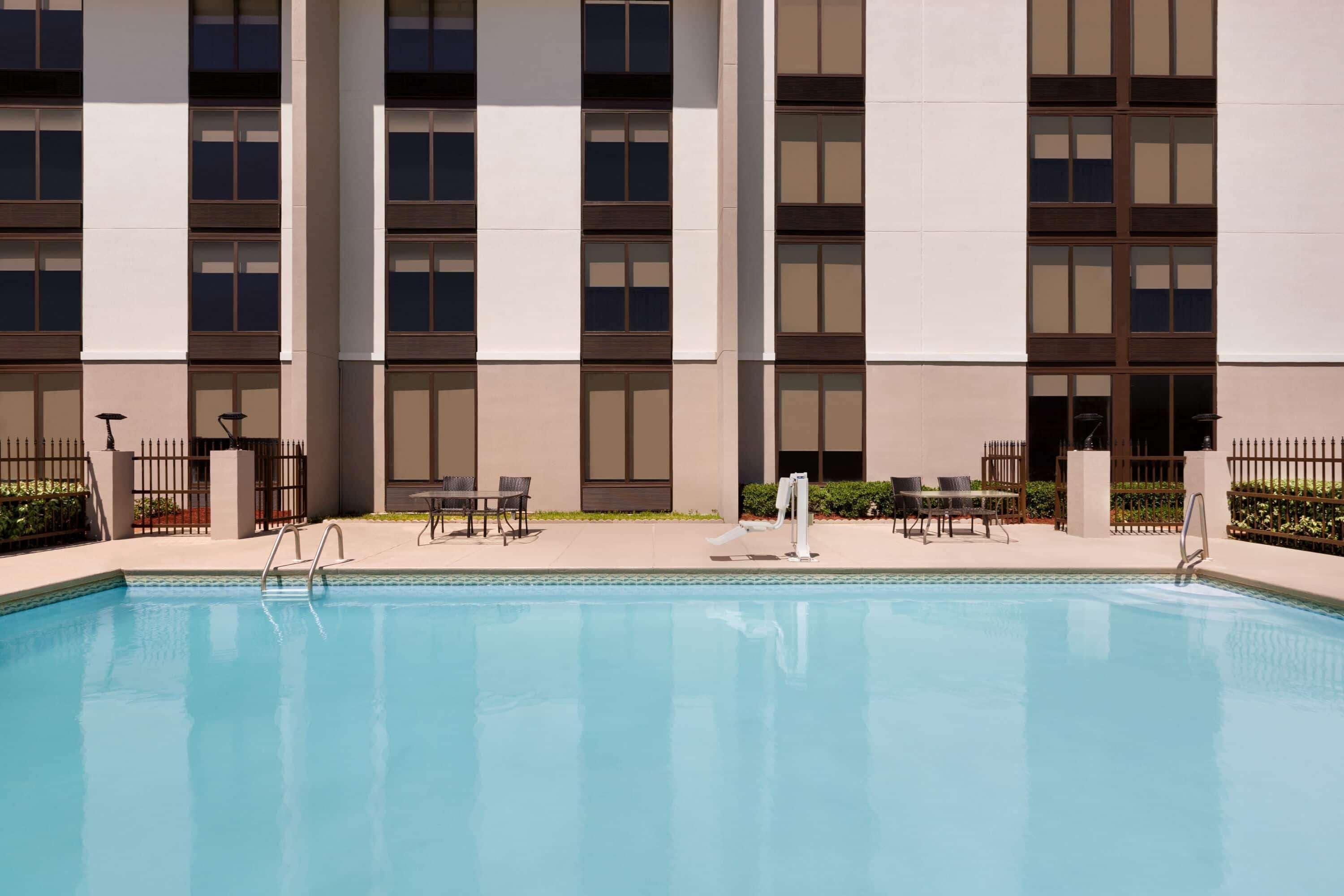 Une piscine avec un bâtiment moderne en arrière-plan, caractérisé par une façade symétrique dotée de grandes fenêtres et d’un toit plat.