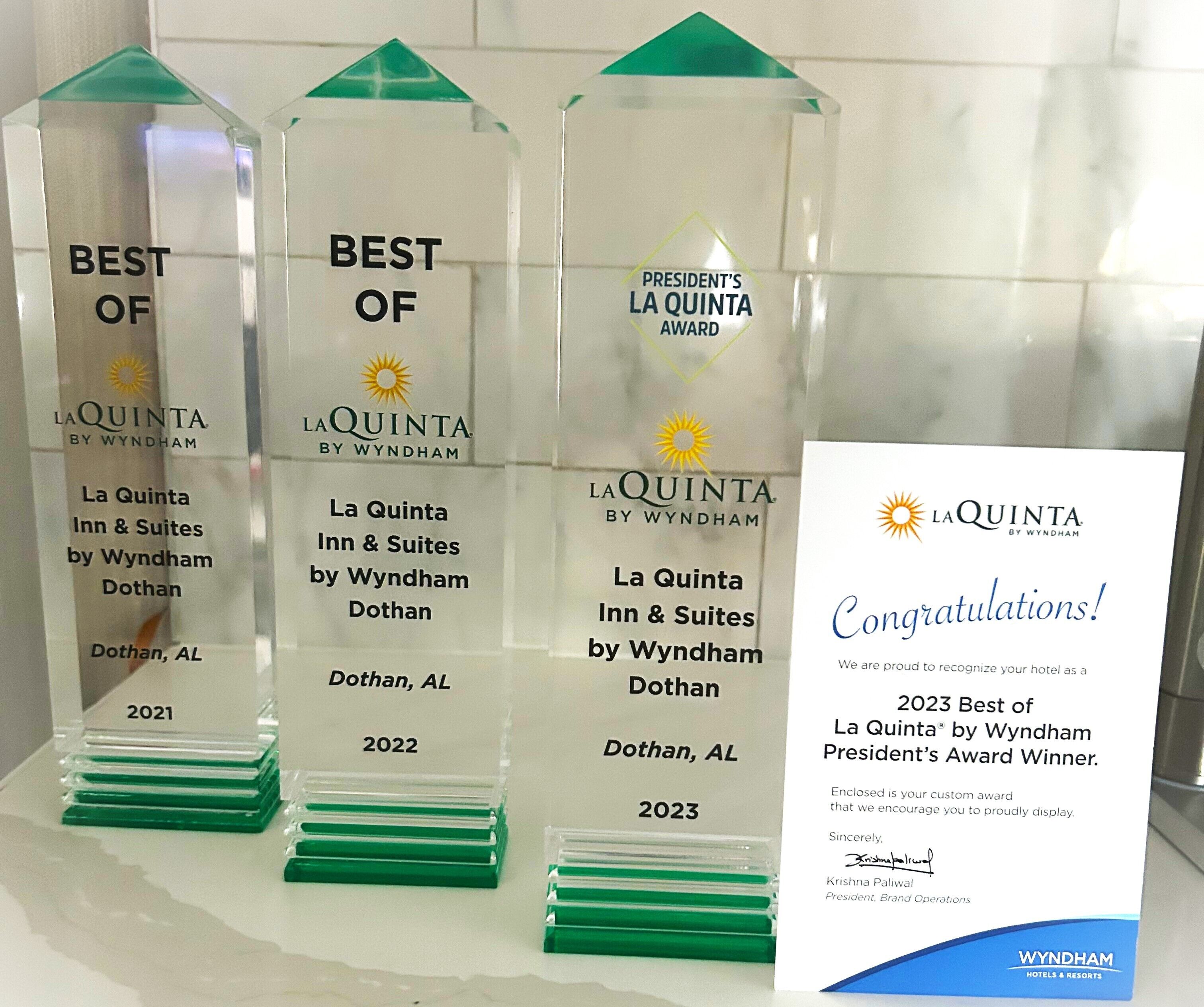 Tres placas de premios para La Quinta Inn & Suites by Wyndham Dothan, AL, con las etiquetas 2021, 2022 y 2023, junto con un certificado de felicitación para el premio de 2023.