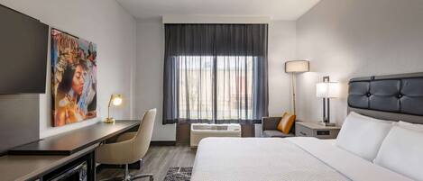 A hotel room with a bed, desk, chair, and artwork on the wall.