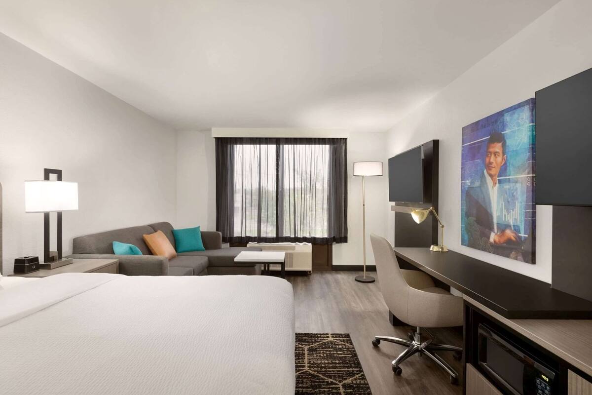 A hotel room with a bed, a desk, a chair, a sofa, a TV, and a window with curtains.