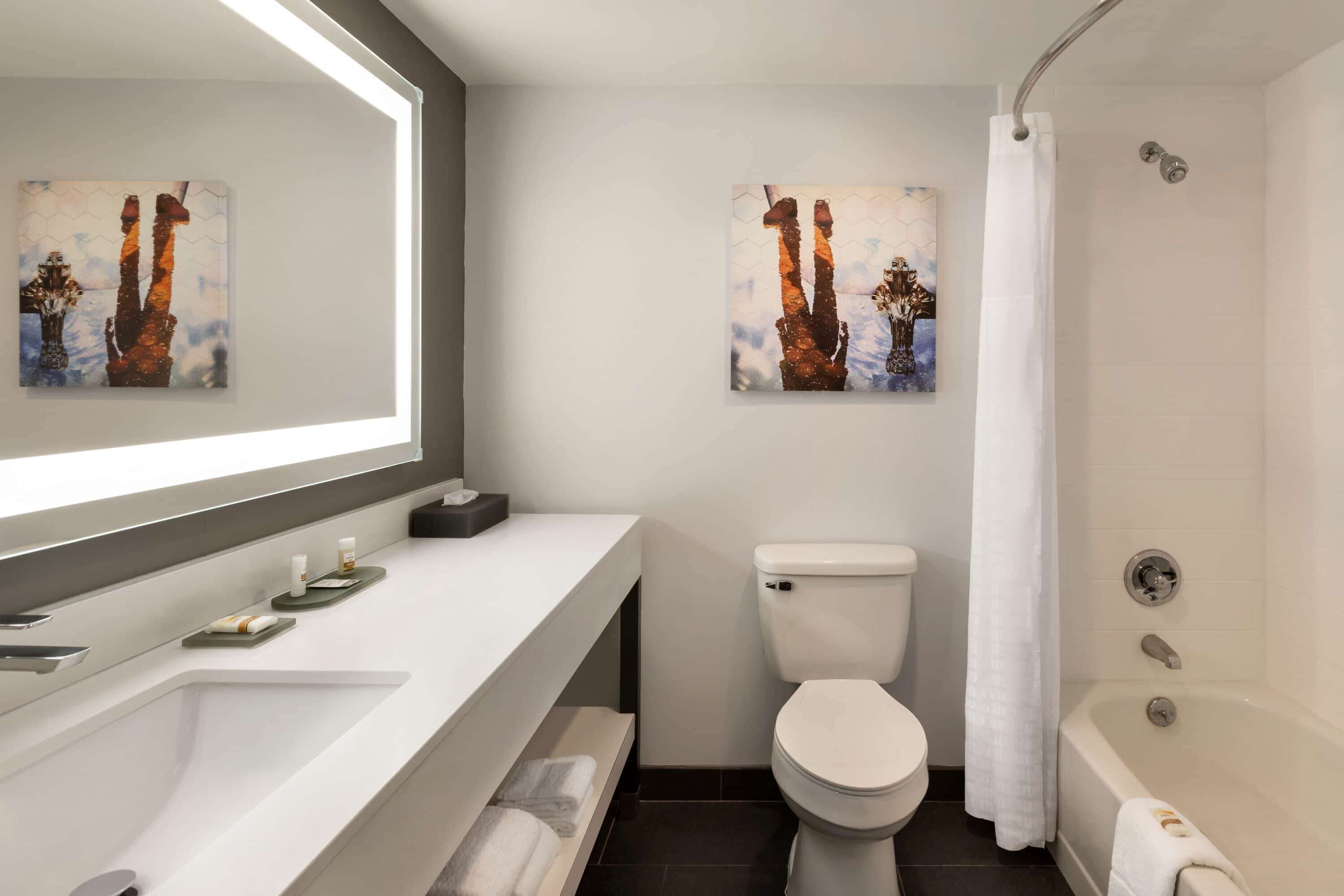 Un baño moderno con lavamanos, inodoro y bañera blancos. Hay dos obras de arte enmarcadas en la pared.