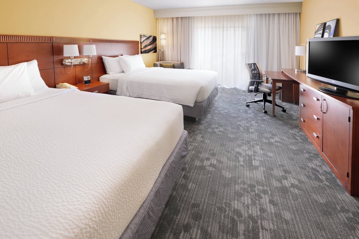 Ein Hotelzimmer mit zwei Betten, einem Schreibtisch, einem Fernseher und einem Sessel.