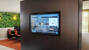 Um painel GoBoard em um saguão de hotel, com uma parede verde coberta de folhagem e cadeiras de escritório vermelhas.
