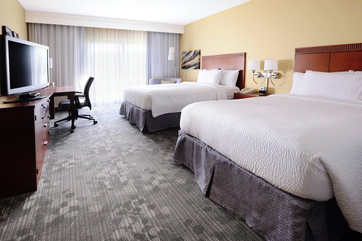 Ein Hotelzimmer mit zwei Betten, einem Schreibtisch, einem Fernseher, einem Sessel und einer Lampe.