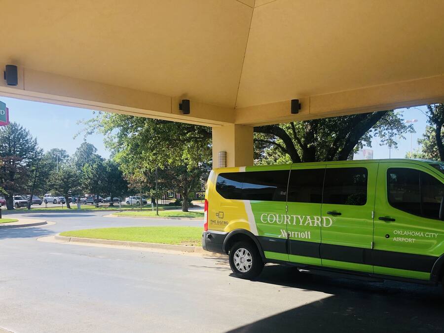 Una furgoneta amb el distintiu de Courtyard Marriott aparcada sota una zona coberta, amb una vista clara dels arbres i la carretera circumdants.