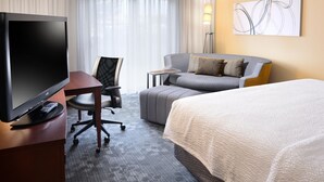 Quarto de hotel com uma cama, uma escrivaninha com televisão, um sofá e uma cadeira.