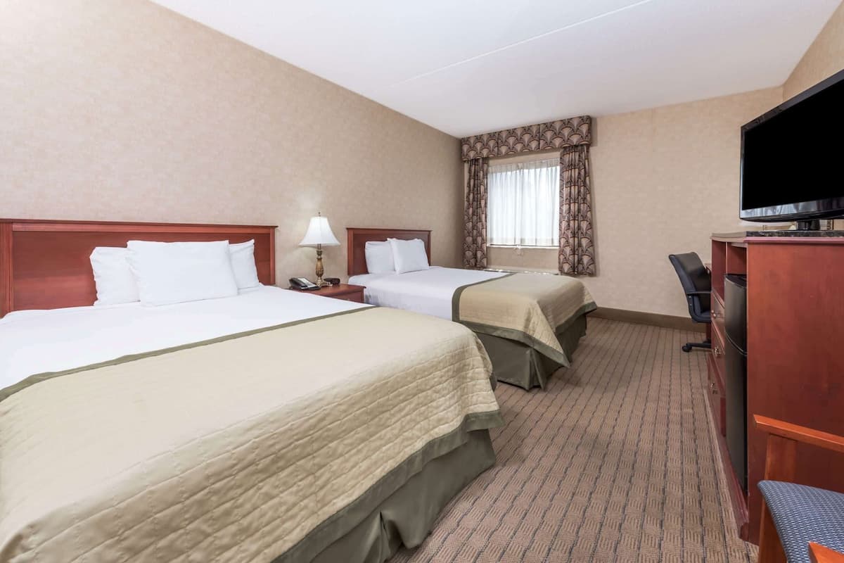 Een hotelkamer met twee bedden, een bureau, een televisie en een raam met gordijnen.