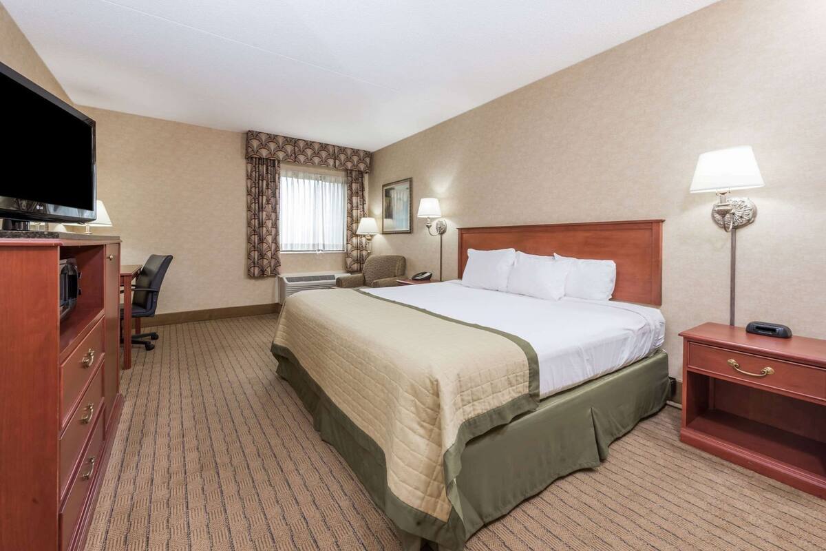 Een hotelkamer met een bed, bureau, stoel, televisie, lamp en telefoon.