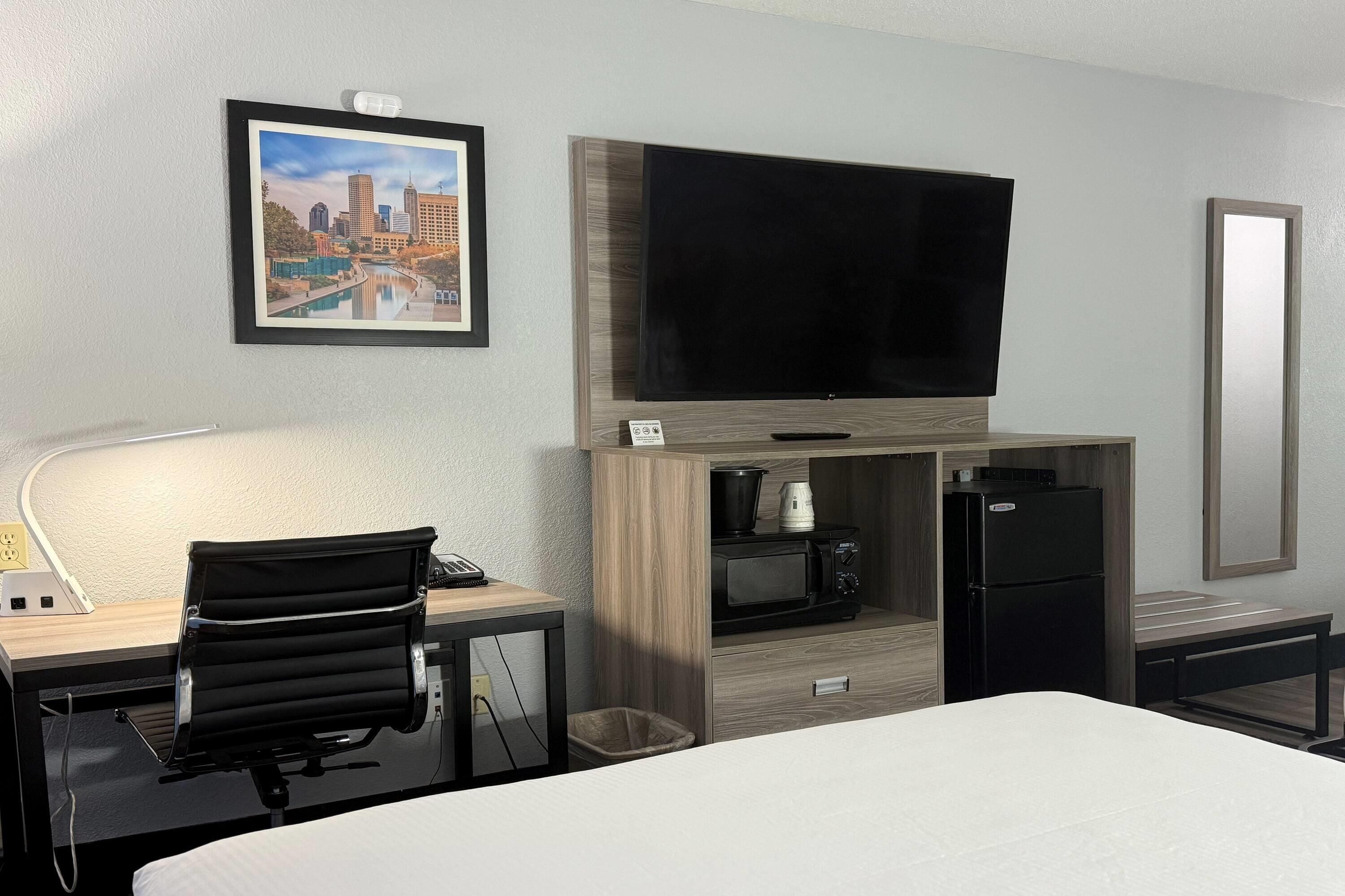 Une chambre d’hôtel comprenant un lit, un bureau avec une chaise, une télévision, un four à micro-ondes, un réfrigérateur et une poubelle.