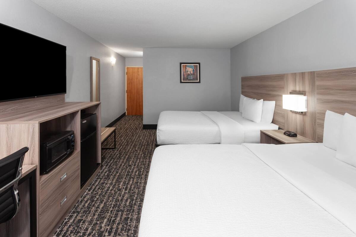Een hotelkamer met twee bedden, een flatscreen-tv, een magnetron, een bureau en een nachtkastje met een lamp.