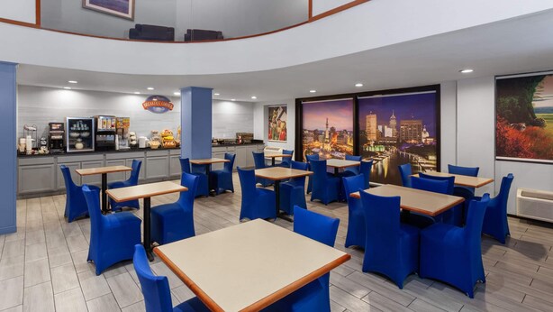 Un restaurant avec des chaises et des tables bleues, un espace cuisine et de grandes fenêtres offrant une vue sur la ville.