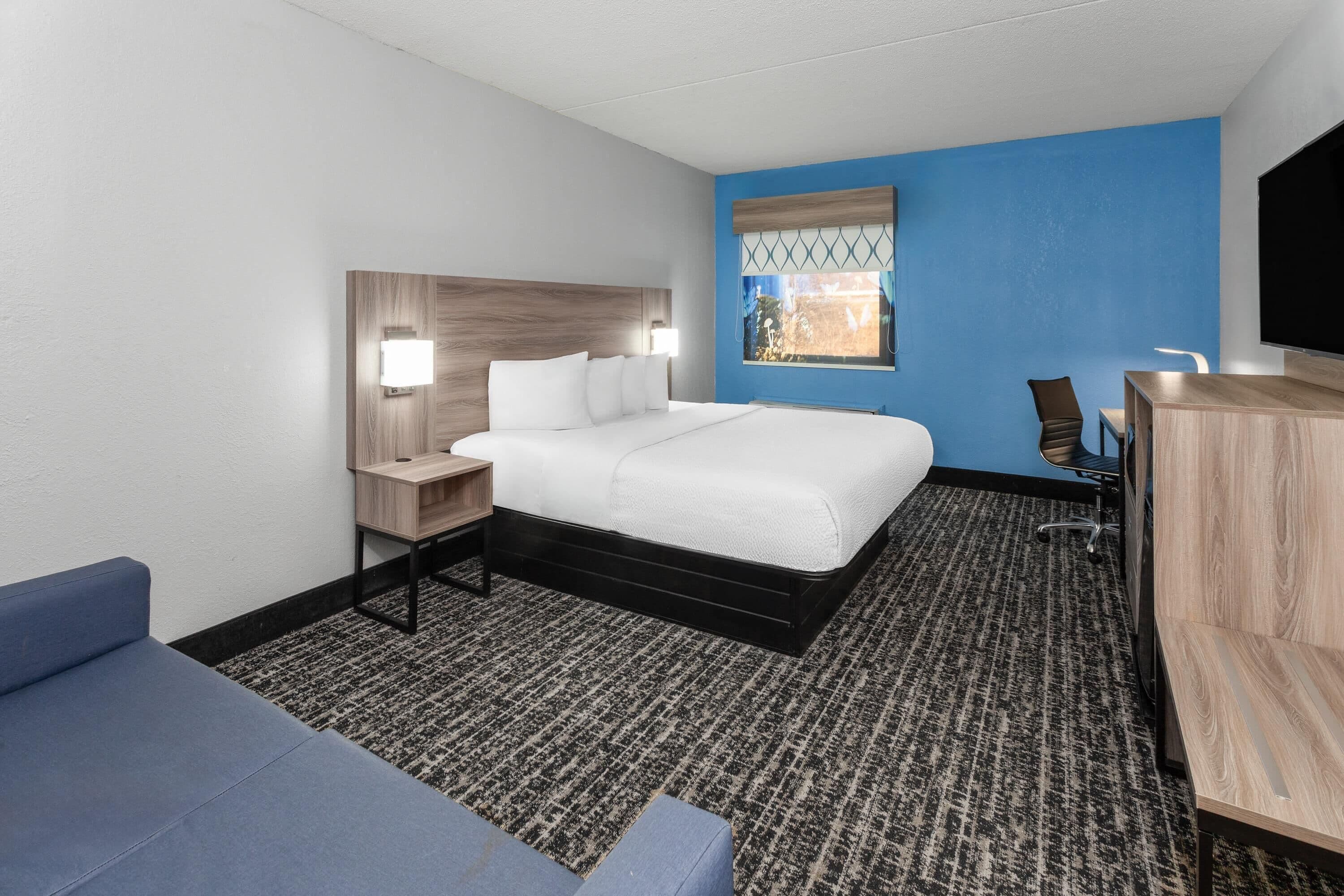 Una habitación de hotel con cama, escritorio, silla, televisor y ventana con vistas.