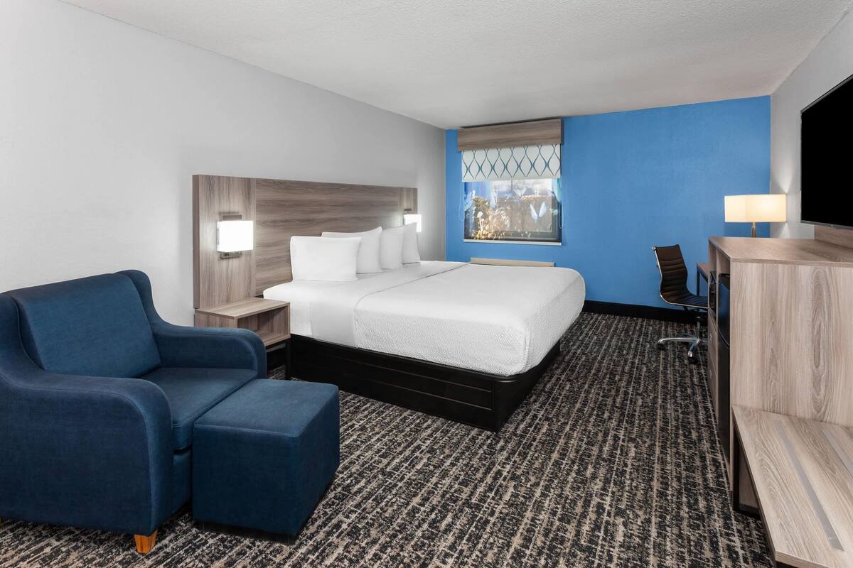Een hotelkamer met een bed, een blauwe fauteuil, een bureau met een lamp en een televisie.
