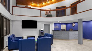 Un hall d'entrée avec des sièges bleus, un comptoir d'accueil, une horloge et un téléviseur fixé au mur.