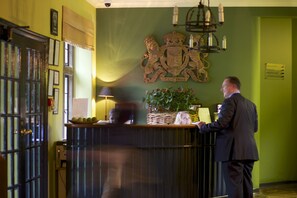 A reception desk with a coat of arms, a lamp, and a plant. - Hare And Hounds Hotel (Tetbury)