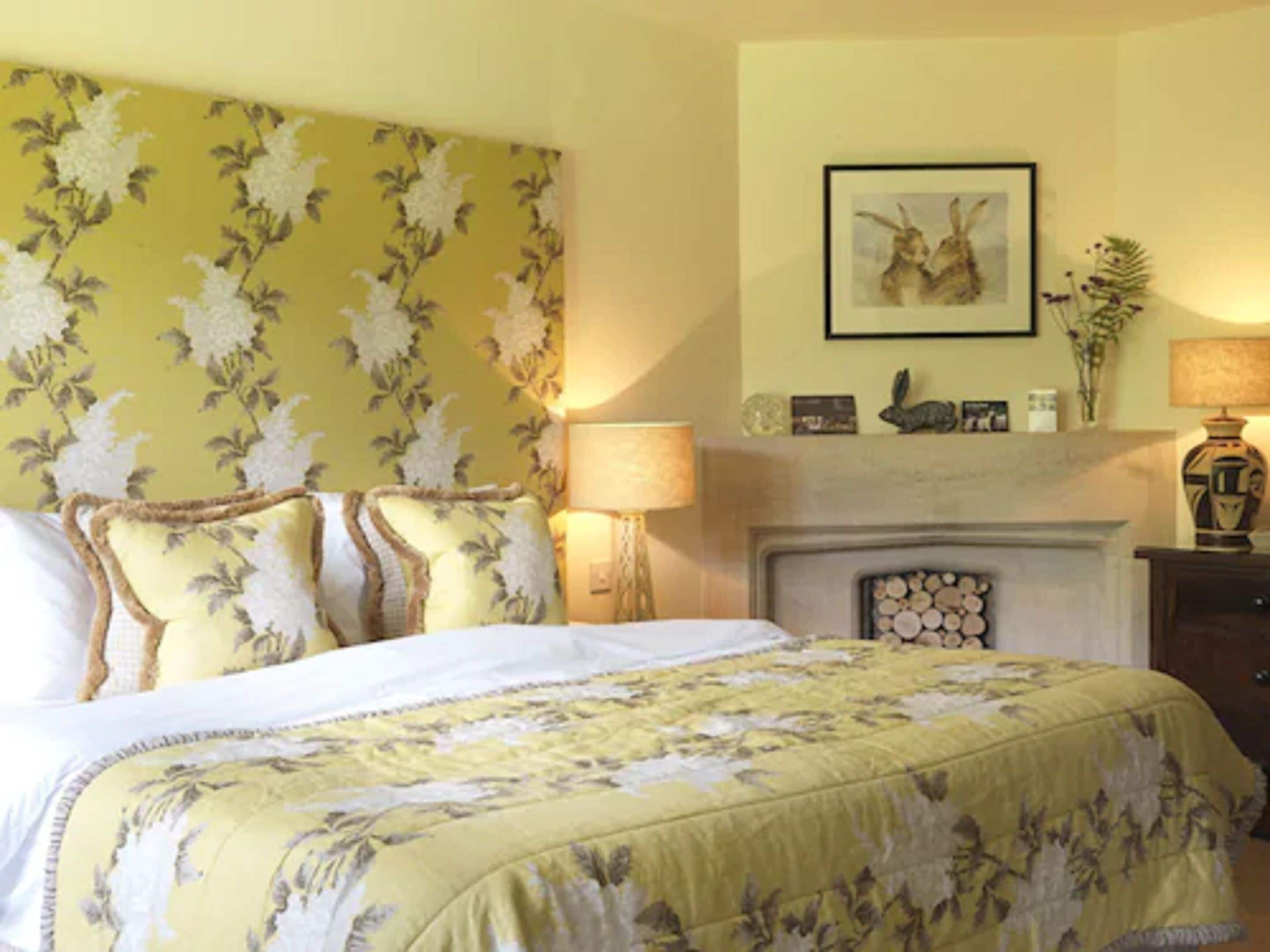A bedroom with a bed, a fireplace, a lamp, and a framed picture on the wall.
