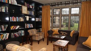 A cozy living room with a fireplace, a bookshelf filled with books, a comfortable sofa, and a plaid armchair. - Hare And Hounds Hotel (Tetbury)
