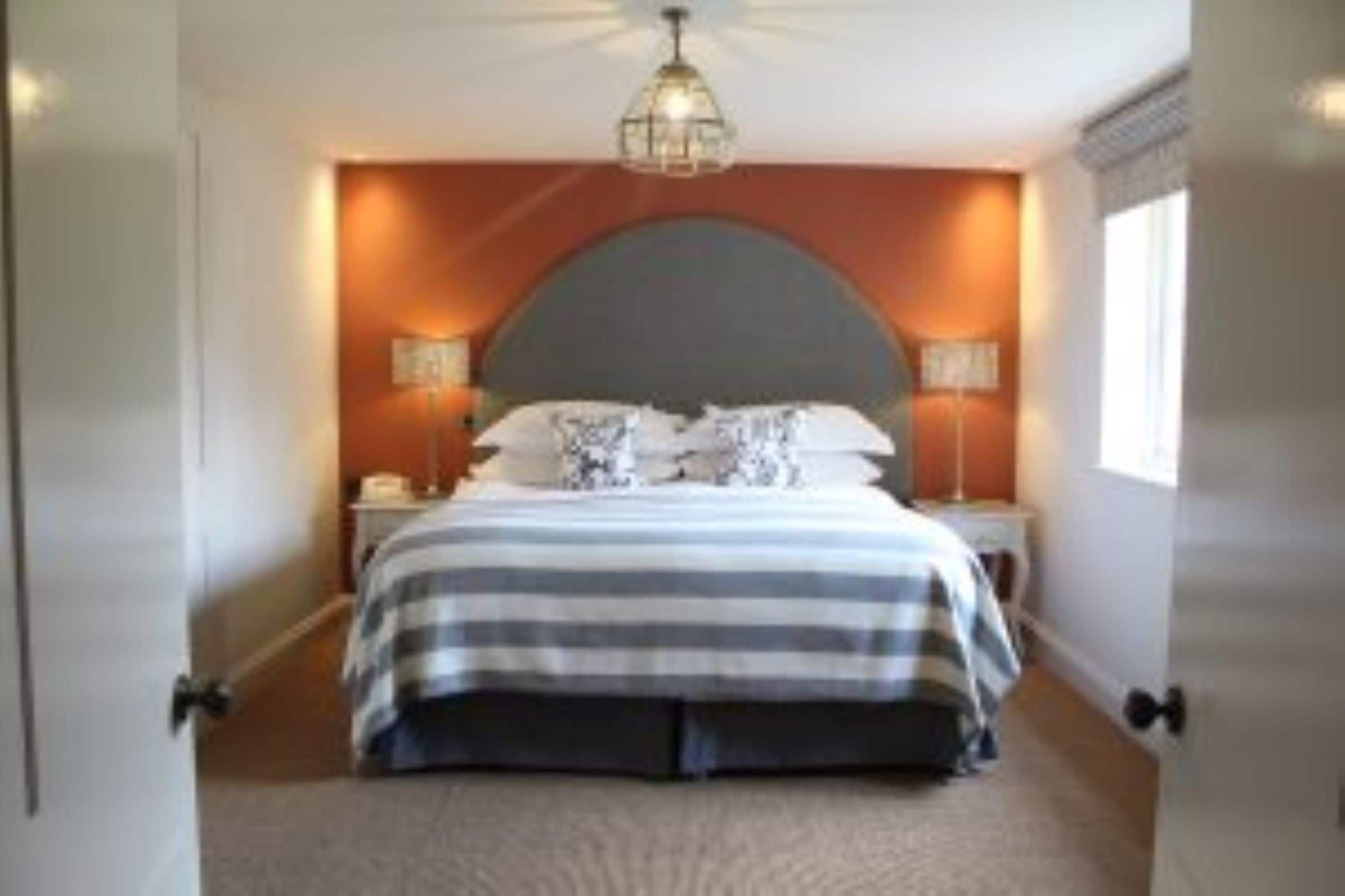 A bedroom with a large bed, a curved headboard, two bedside tables with lamps, and a hanging light fixture.
