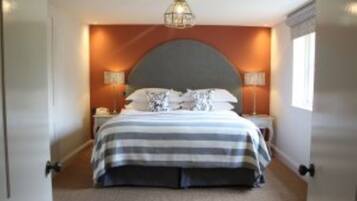 A bedroom with a large bed, a curved headboard, two bedside tables with lamps, and a hanging light fixture.
