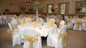 A banquet hall with round tables, white tablecloths, and chairs with gold sashes.