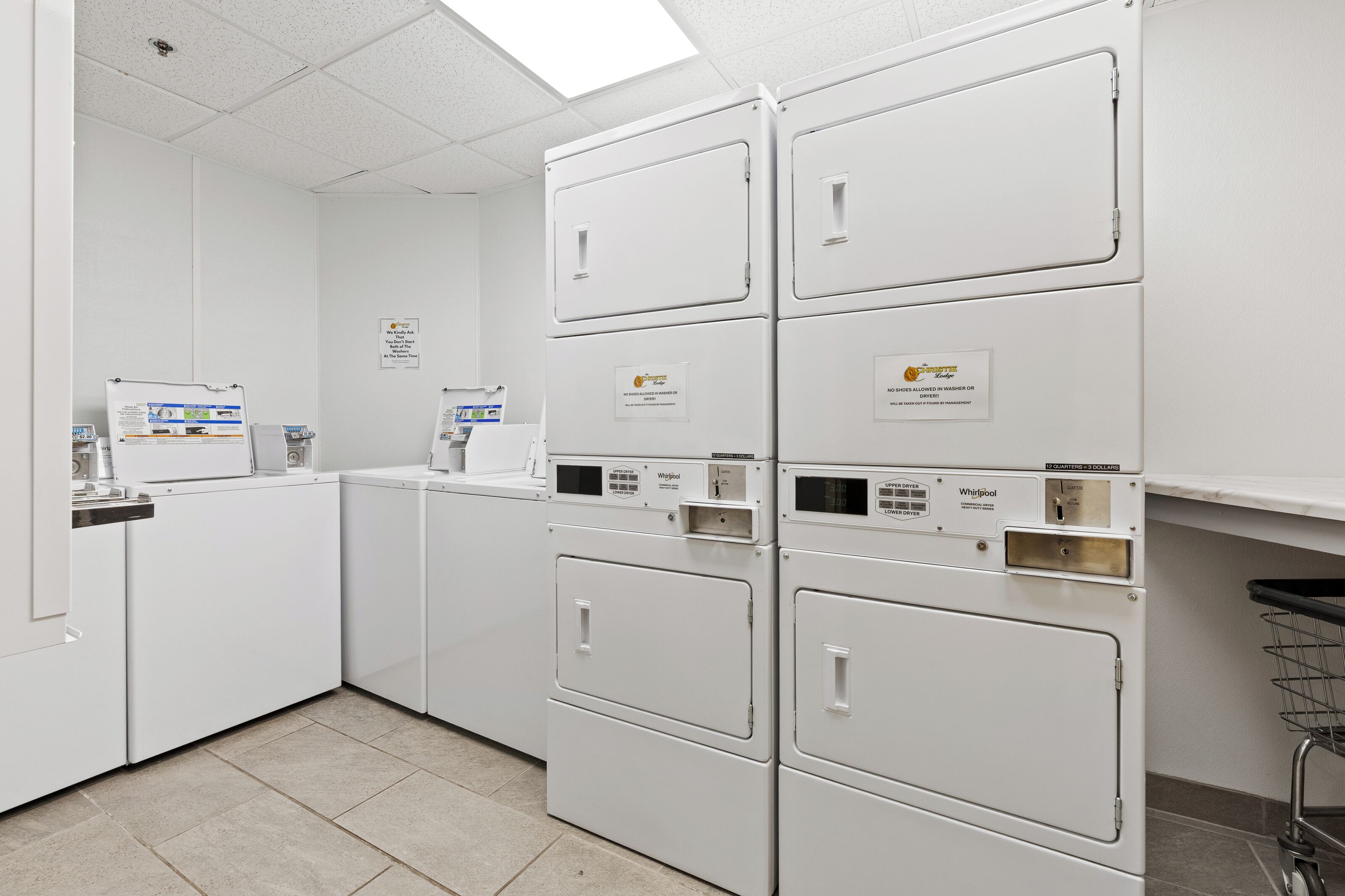A laundry facility with multiple washers and dryers, including a sign prohibiting shoes in the machines.