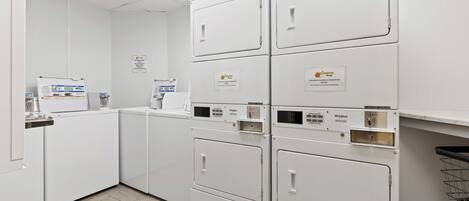 A laundry facility with multiple washers and dryers, including a sign prohibiting shoes in the machines.
