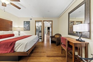 Habitación de hotel con cama de madera, un escritorio con silla, un espejo grande y vista al pasillo.