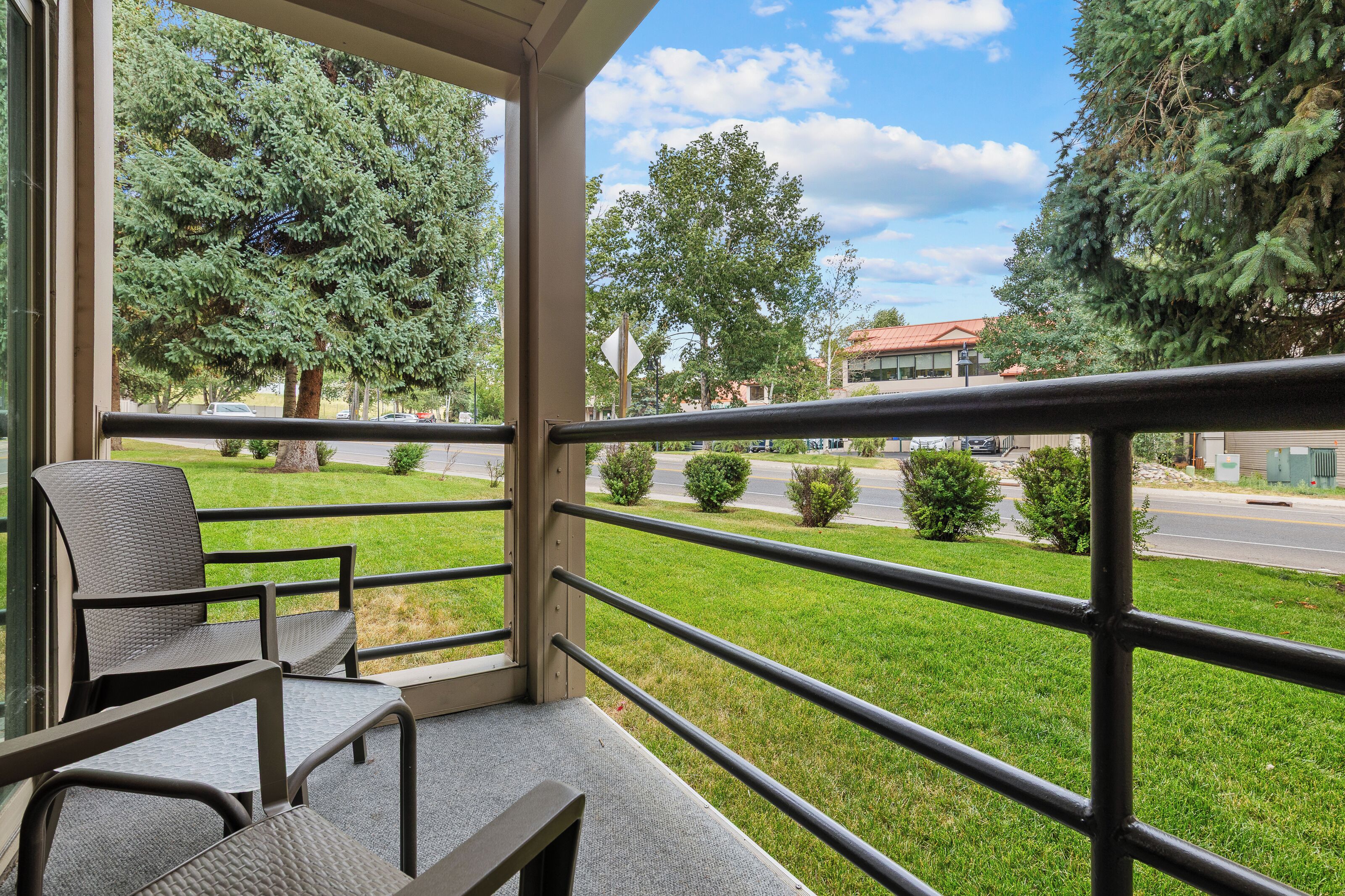 Ein Balkon mit Blick auf eine grüne Wiese, Bäume und eine Straße.