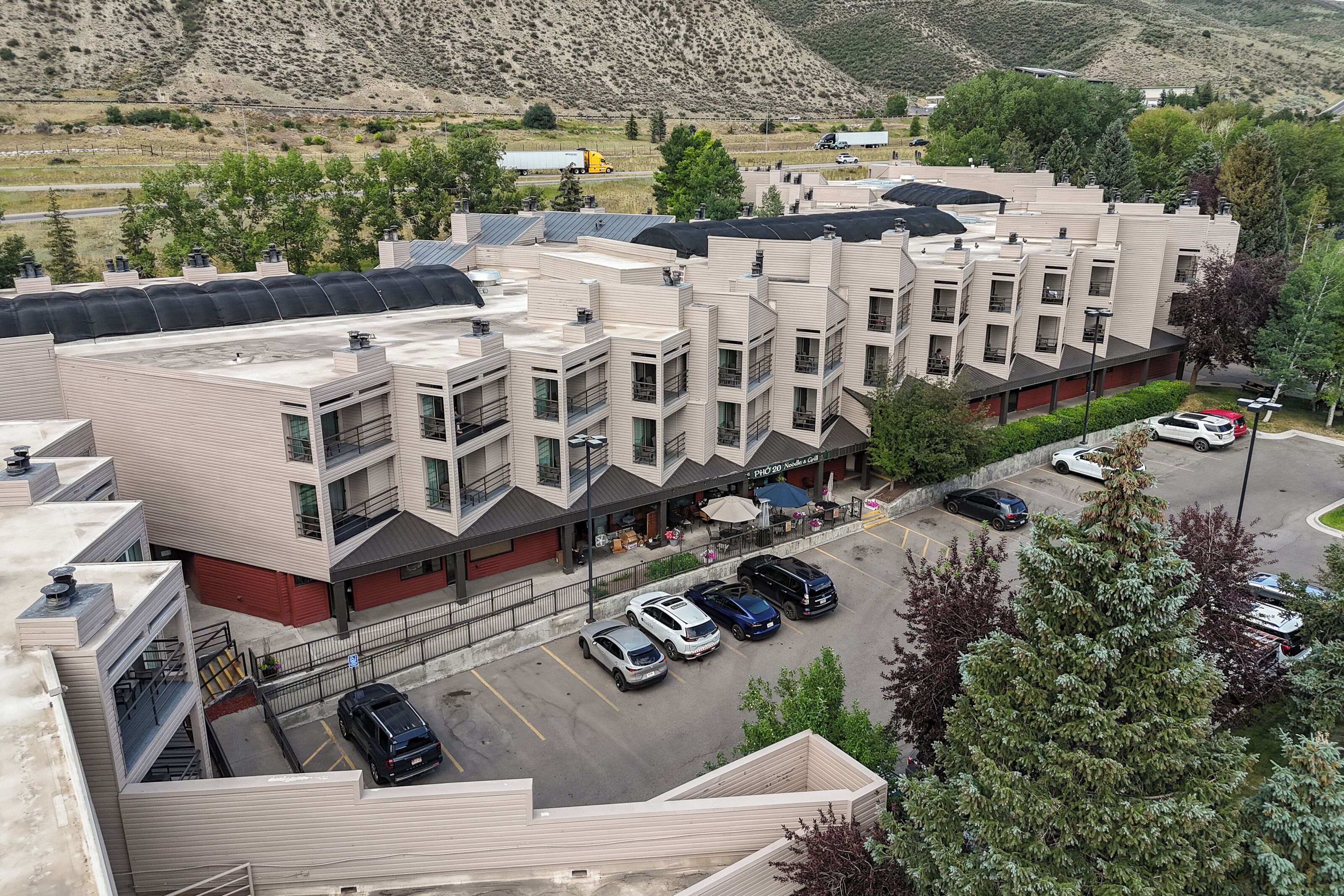 Een meerlaags hotel met een modern architectonisch ontwerp, met een parkeerplaats met meerdere auto's en een uitzicht op het omliggende landschap.