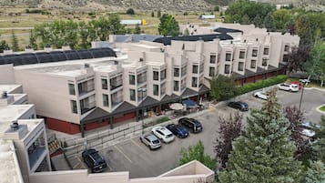 Een meerlaags hotel met een modern architectonisch ontwerp, met een parkeerplaats met meerdere auto's en een uitzicht op het omliggende landschap.