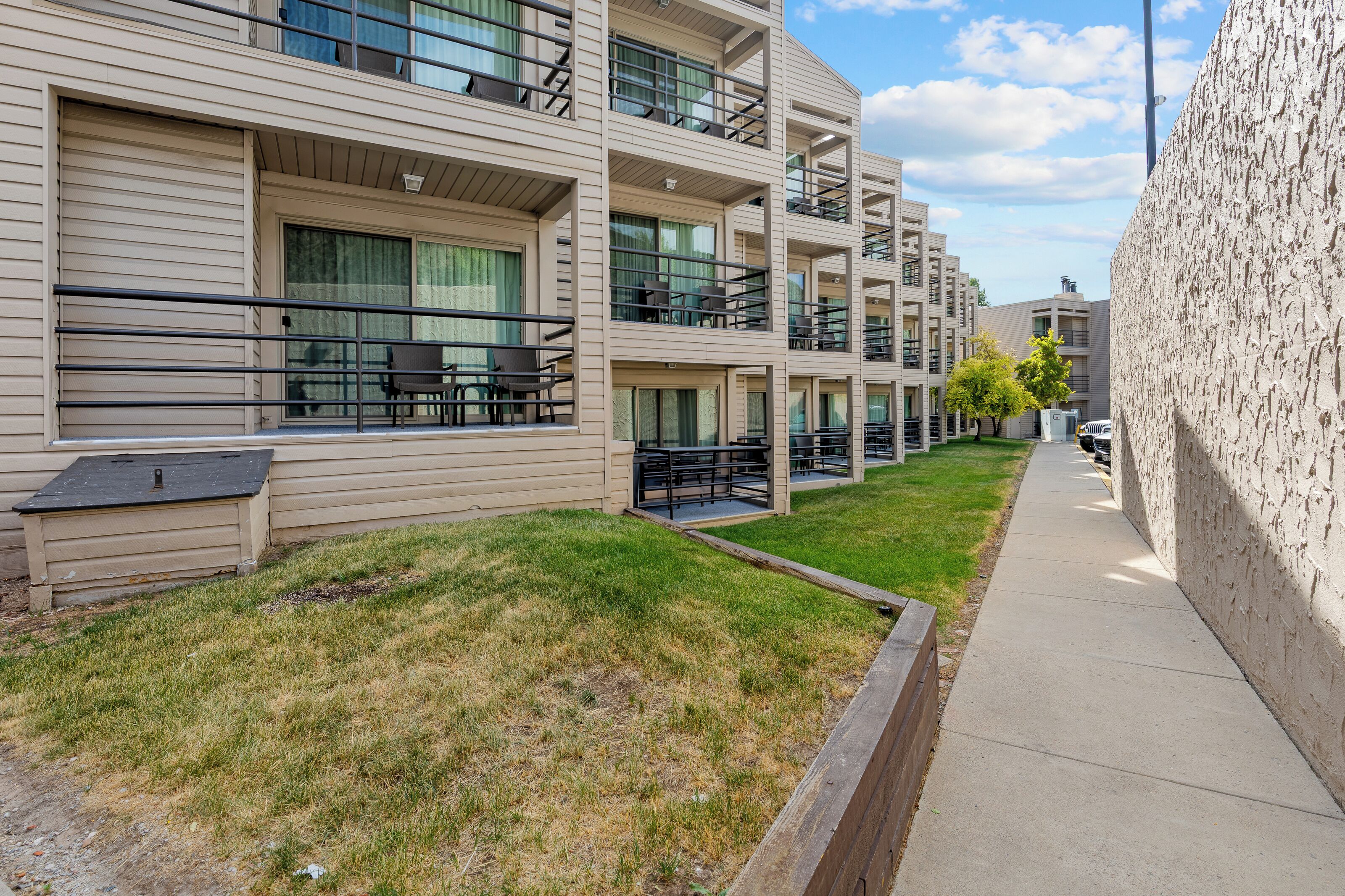 A multi-story residential building with balconies, a grassy area, and a sidewalk.