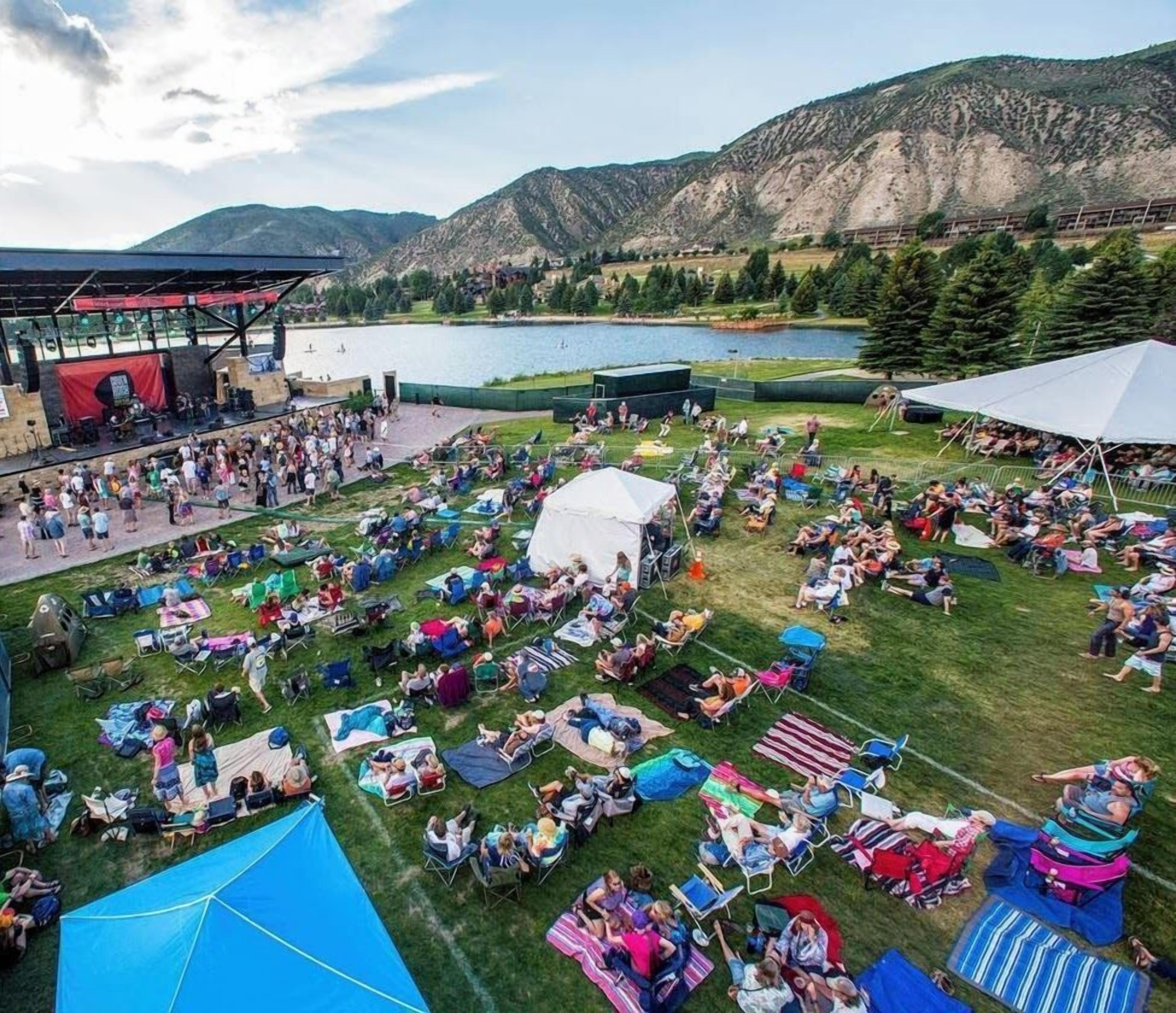 An outdoor event with a stage and audience, set against a mountainous backdrop.