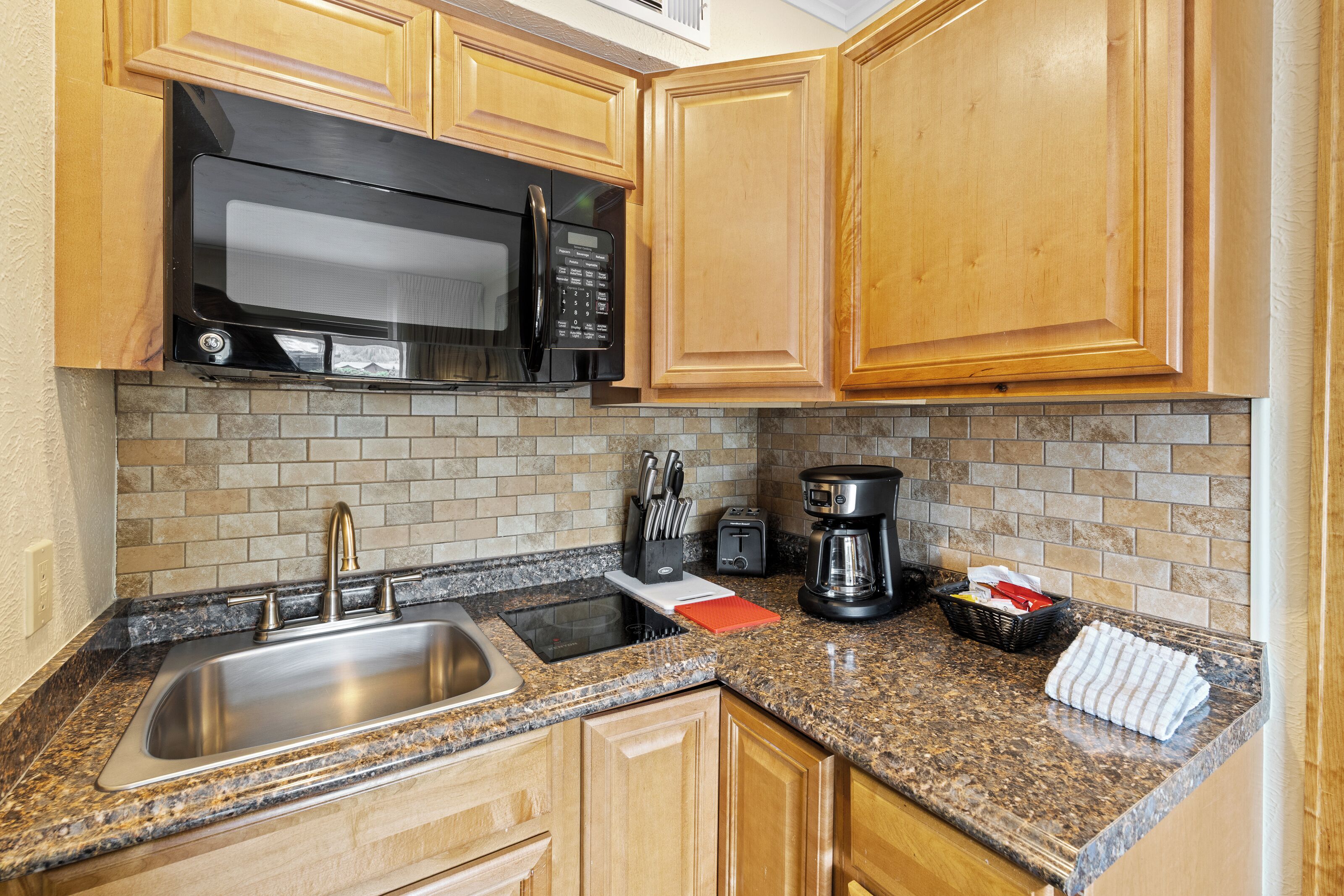 A kitchen with wooden cabinets, a stainless steel sink, a microwave, a toaster, and a coffee maker.