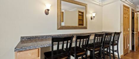 A kitchen with a granite countertop, four dark wooden chairs, and a large mirror above the counter.