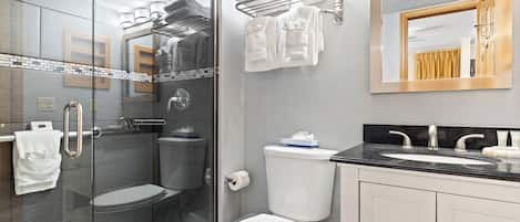 A modern bathroom with a glass shower enclosure, a white toilet, a sink with a black countertop, and a mirror above the sink.