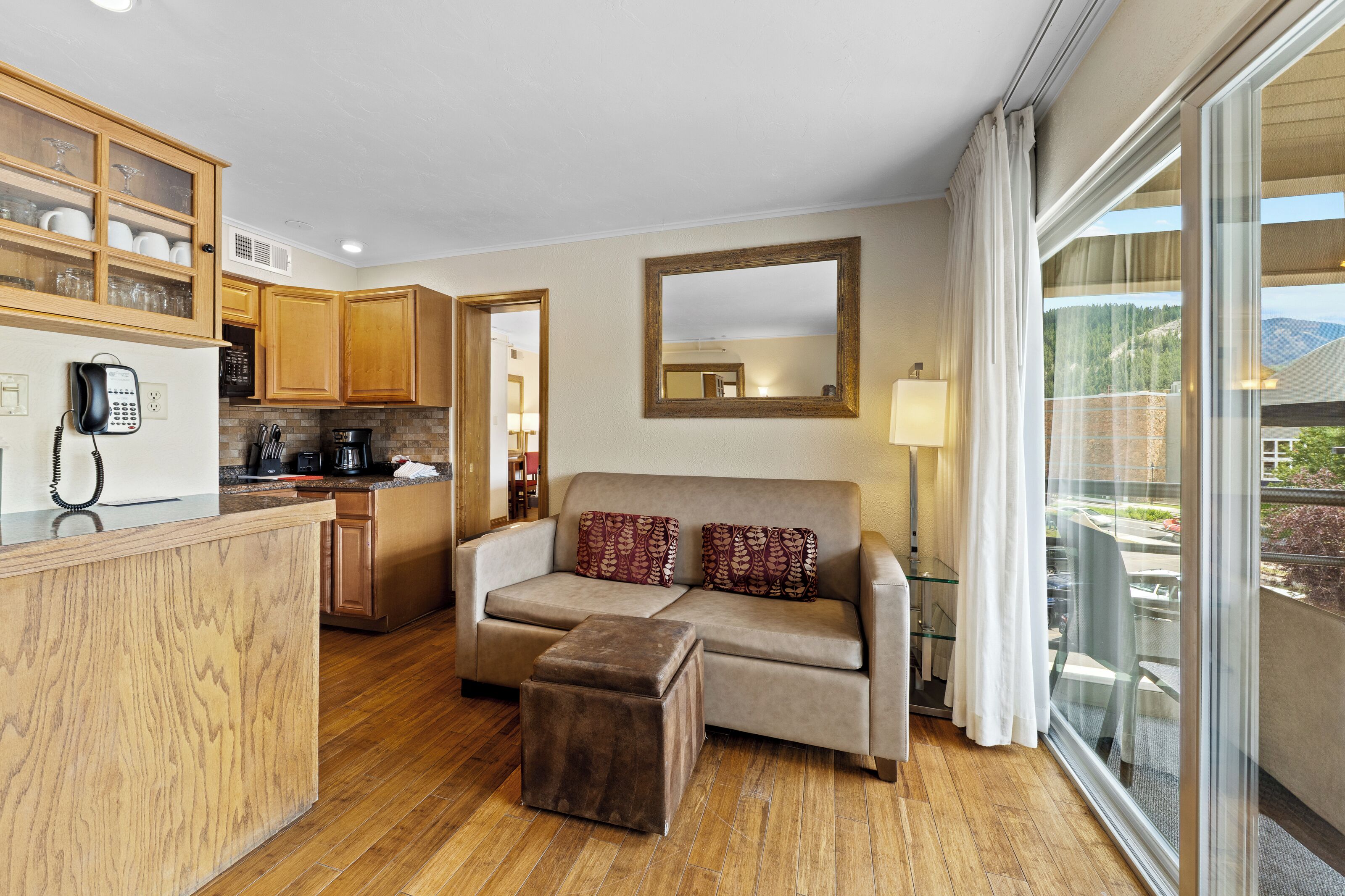 Een moderne woonkamer met een bank, een poef en een eetgedeelte met houten kasten en een keuken.