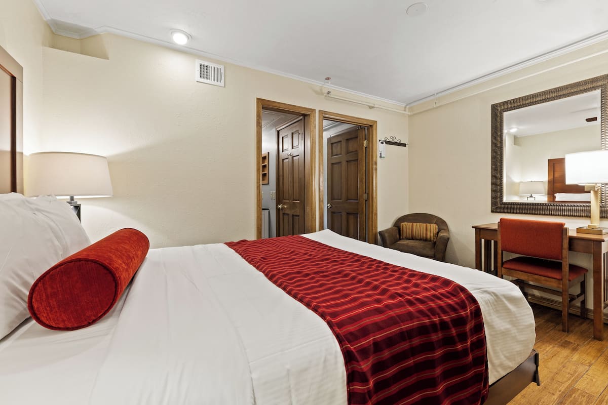 A hotel room with a bed, a desk, a chair, and a mirror.