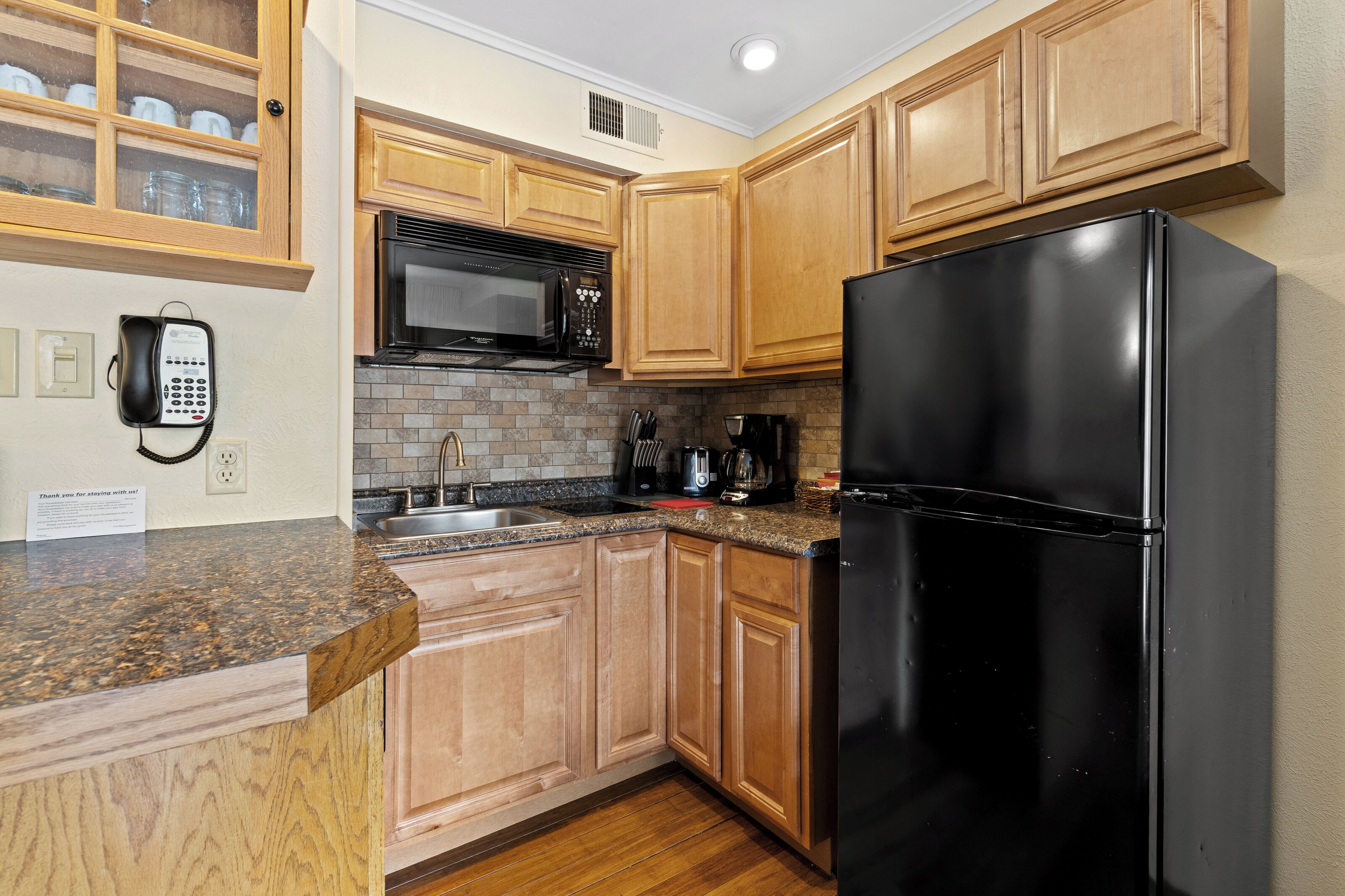 A kitchen with wooden cabinets, a black refrigerator, a microwave, and a sink.