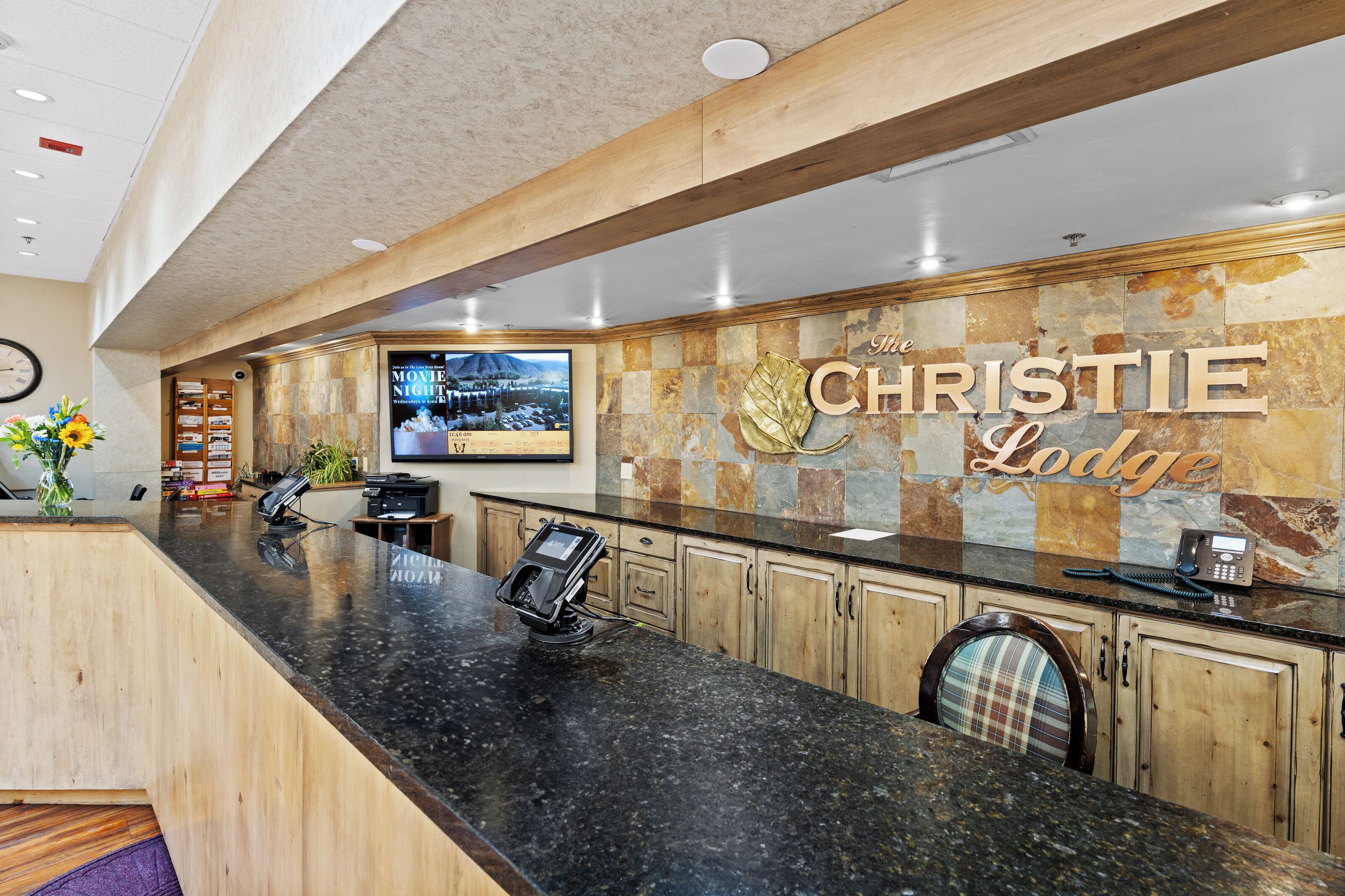 A reception area with a black granite counter, wooden cabinets, a mounted television, and a sign reading "The Christie Lodge".