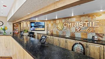 A reception area with a black granite counter, wooden cabinets, a mounted television, and a sign reading "The Christie Lodge".