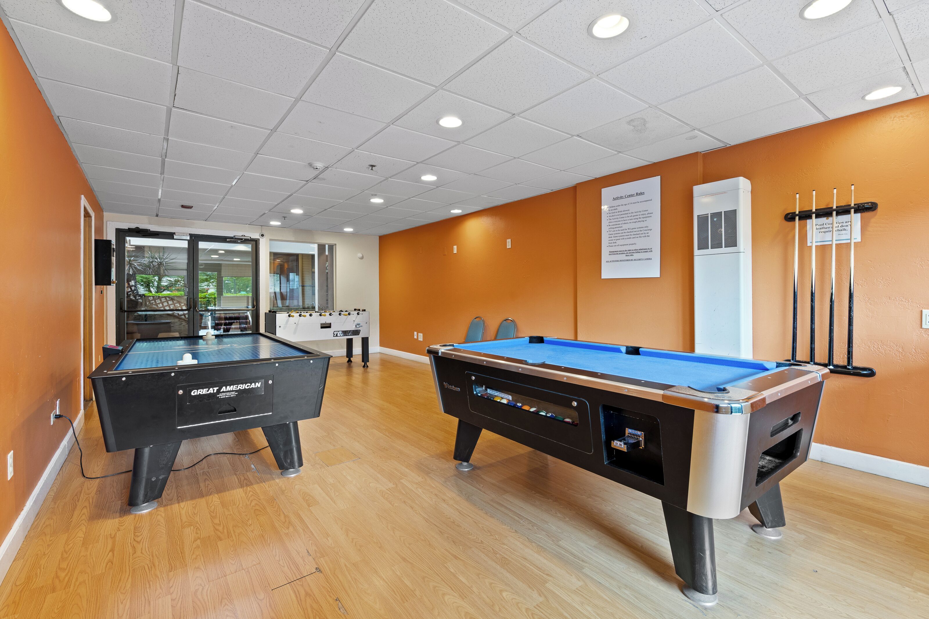 A pool table area with two pool tables, a billiard cue rack, and a wall-mounted air conditioning unit.