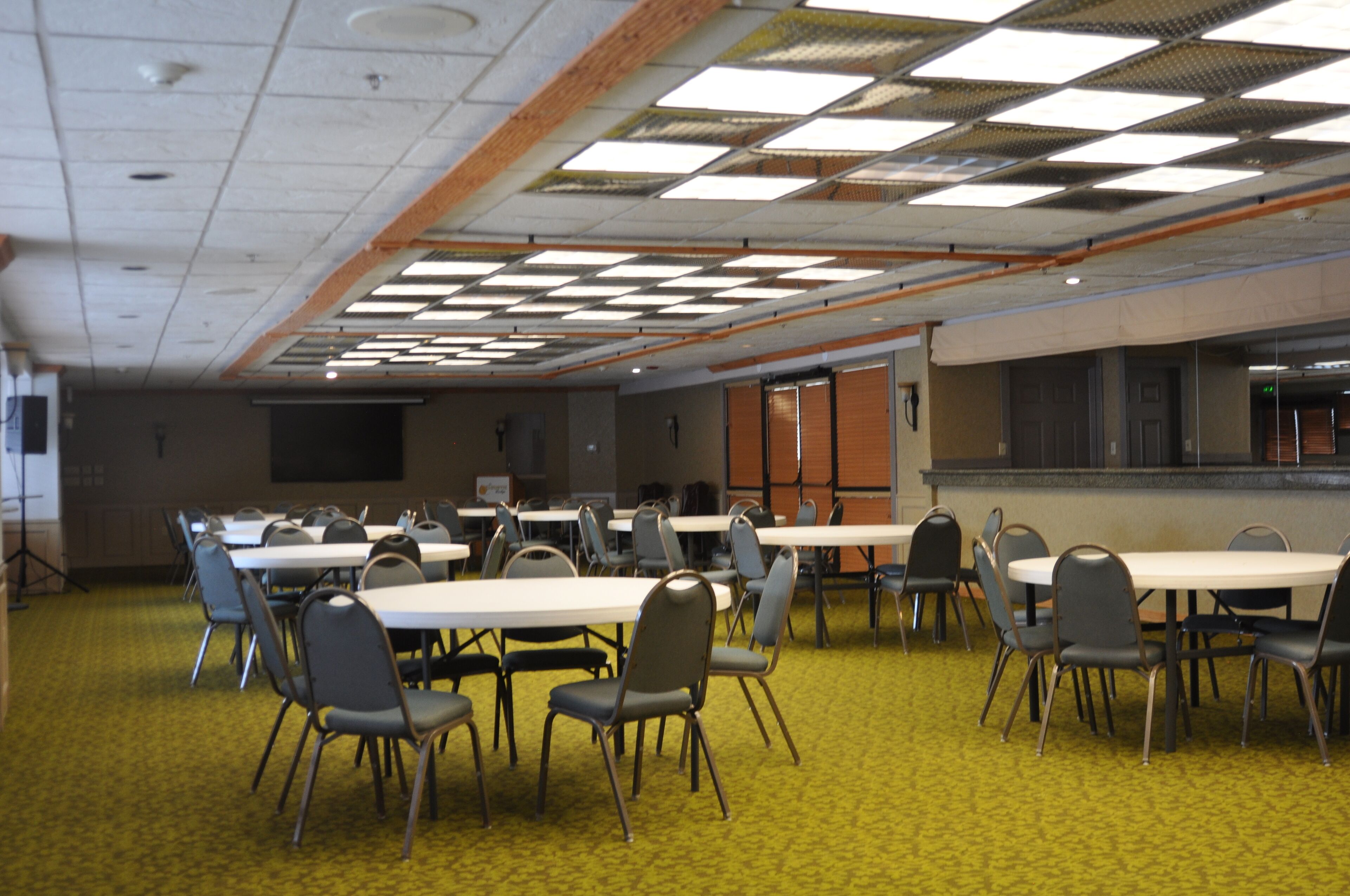 A conference room with multiple tables and chairs, carpeted floor, and a ceiling with fluorescent lights.