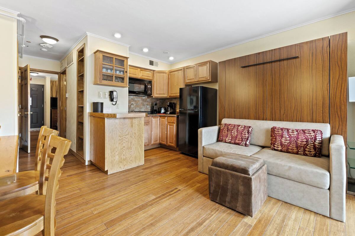 A compact living space with a kitchenette, wooden flooring, a sofa, and a dining area.